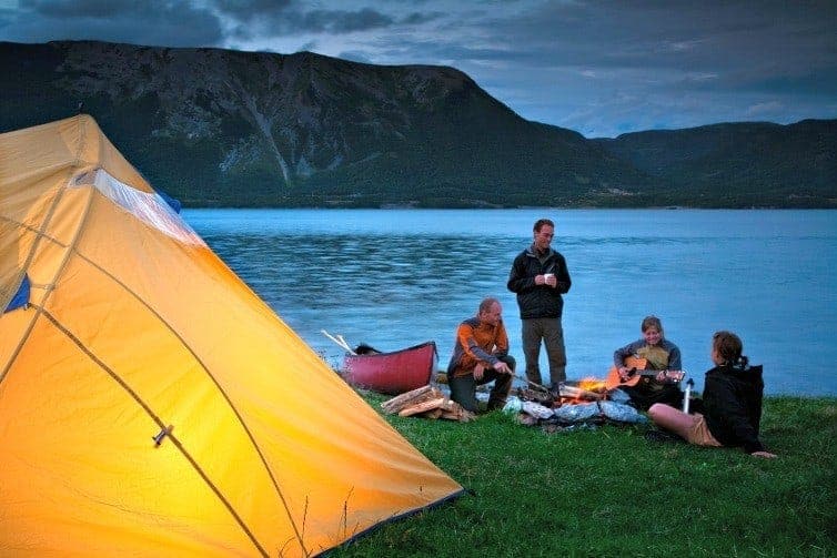camper in canada sitting by lake strumming guitar