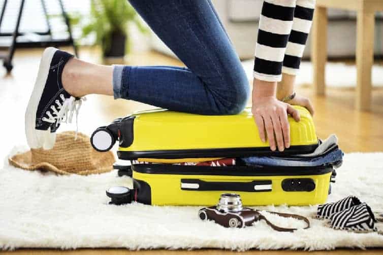 lady kneeling on suitcase to pack items for trip